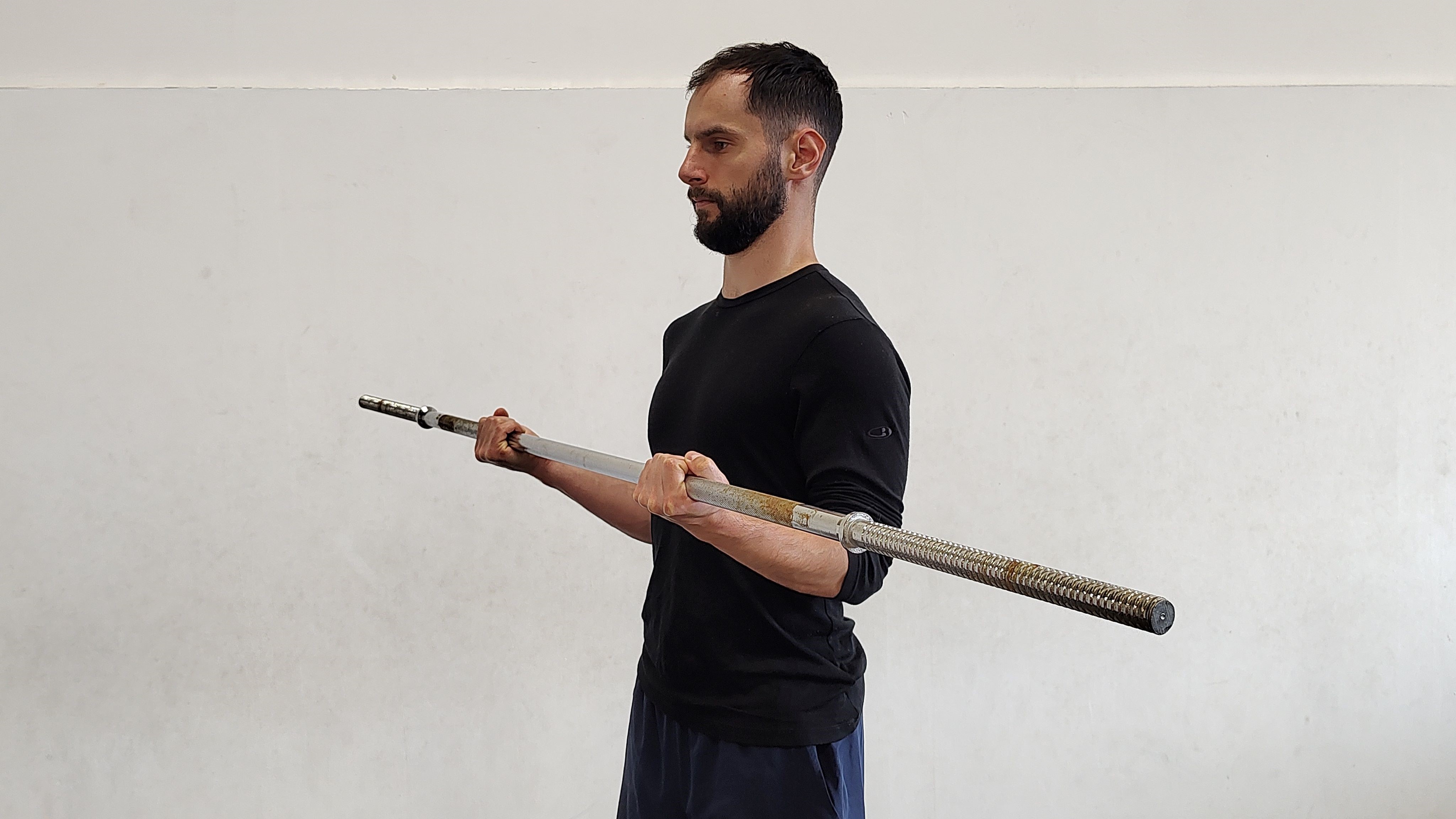 Muž cvičí v tělocvičně bicepsový zdvih s osou s podhmatem.
